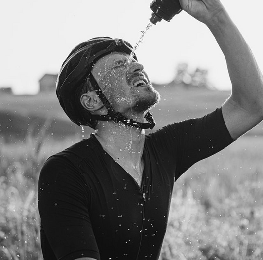 Ciclista com bidon de água na mão a molhar o rosto para se hidratar